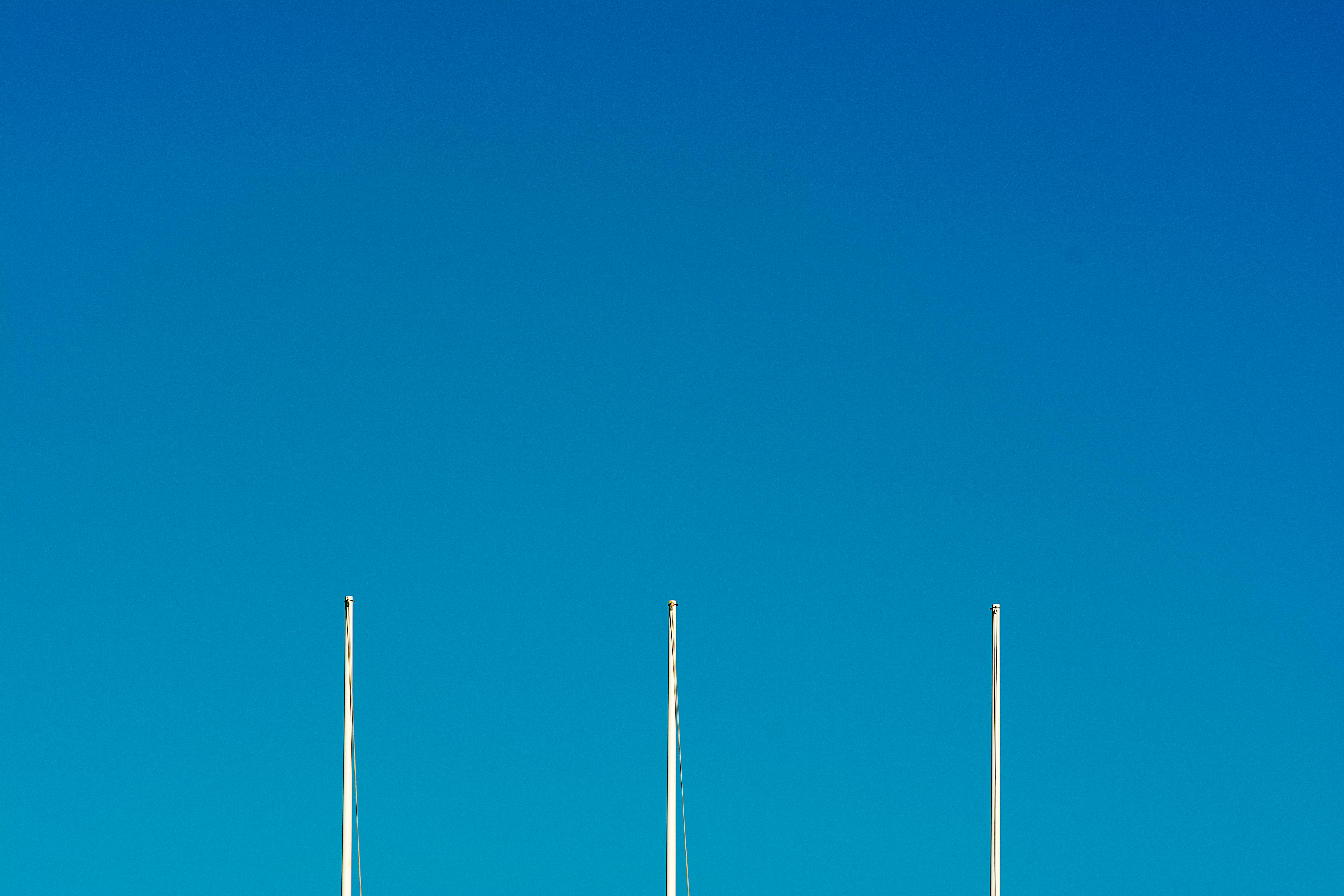 A clear blue sky with three vertical poles creates a minimalist composition, emphasizing simplicity and open space.